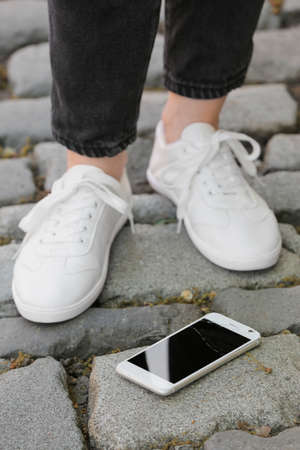 Legs of woman and damaged mobile phone on paving stones outdoors, closeup