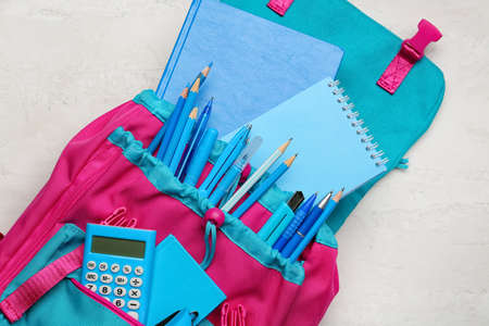 School backpack and stationery on light background