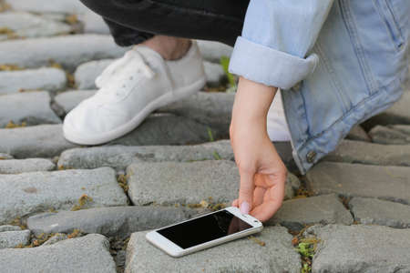 Woman picking damaged mobile phone from paving stones outdoors, closeupの写真素材
