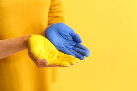 Woman with painted palms in colors of Ukrainian flag on yellow background, closeupの写真素材
