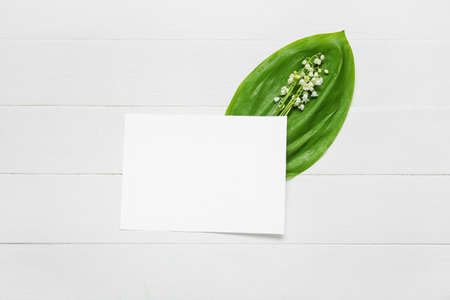 Beautiful lily-of-the-valley flowers and blank card on light wooden background