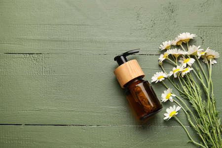 Bottle of essential oil and chamomile flowers on color wooden backgroundの写真素材