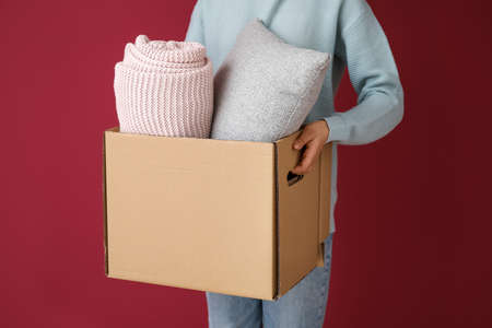 Woman holding box with plaid and pillow on color backgroundの写真素材