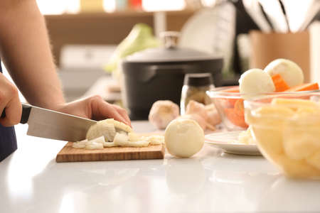 Young woman cutting onion for delicious borscht on wooden table in kitchen