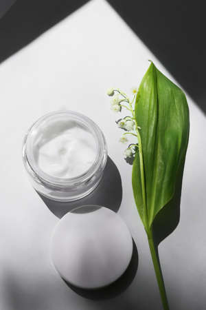 Jar of cream and lily-of-the-valley flowers on light backgroundの写真素材
