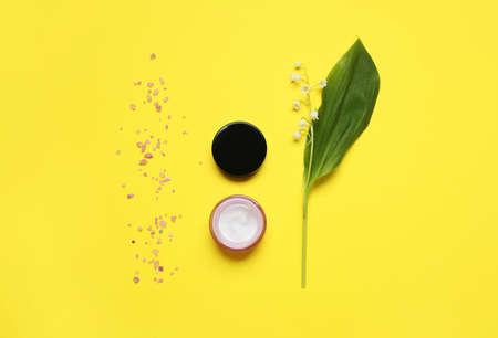 Jar of cream, sea salt and lily-of-the-valley flowers on color backgroundの写真素材