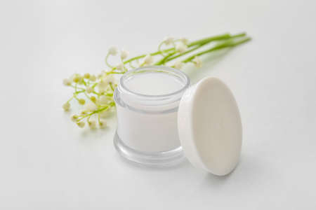 Jar of cream and lily-of-the-valley flowers on light backgroundの写真素材
