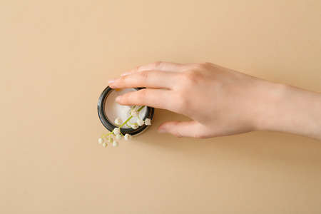 Female hand, jar of cream and lily-of-the-valley flowers on color backgroundの写真素材