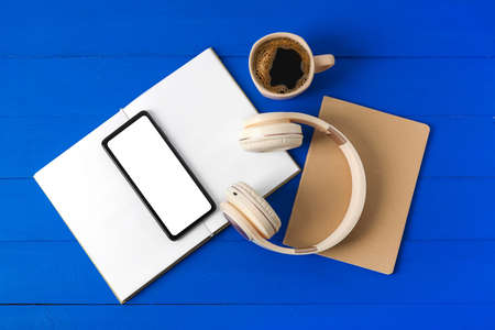 Modern mobile phone, headphones, book and cup of coffee on color wooden background