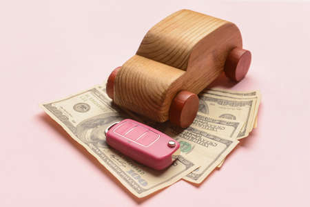 Wooden car with key and banknotes on pink background