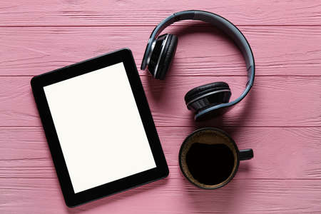 Modern tablet computer, cup of coffee and headphones on color wooden background