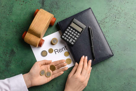 Woman with coins, word RENT, wooden car and stationery on grunge backgroundの写真素材