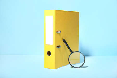 Office folder and magnifying glass on color background