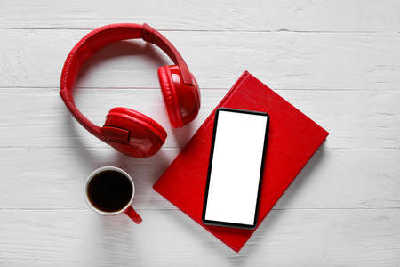 Modern mobile phone, headphones, book and cup of coffee on light wooden backgroundの写真素材