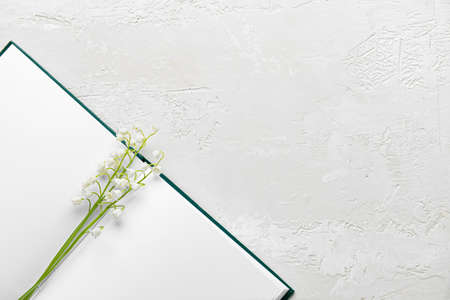 Blank book and beautiful lily-of-the-valley flowers on light background