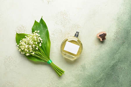 Bottle of perfume and lily-of-the-valley flowers on light background
