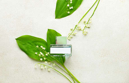 Bottle of perfume and lily-of-the-valley flowers on light background