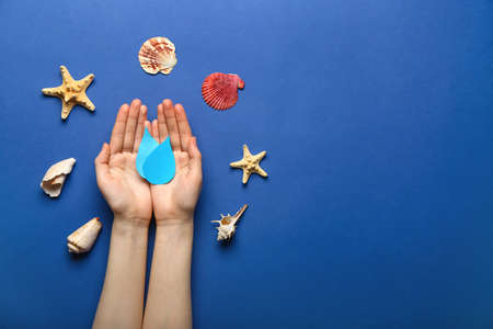 Human hands with paper water drops and sea shells on color background. Ecology concept