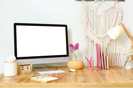 Computer with blank screen, stationery and lamp on desk near light wall