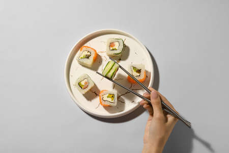 Woman taking delicious sushi roll from plate on light background