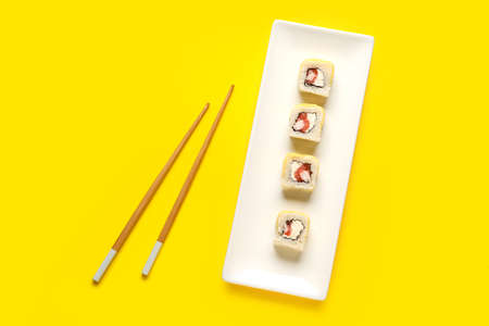 Plate with delicious sushi rolls and wooden chopsticks on color background