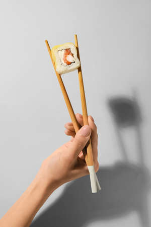 Woman holding wooden chopsticks with delicious sushi roll on light backgroundの写真素材