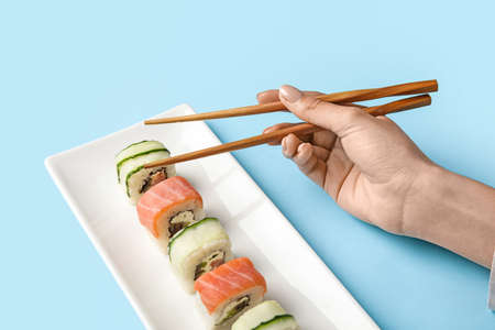 Woman eating delicious sushi rolls on color background, closeup