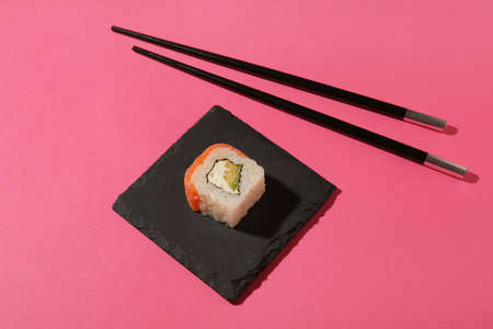 Board with delicious sushi roll and chopsticks on color background