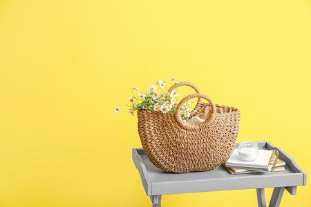 Bag with chamomiles, candle and notebooks on table near color wallの写真素材