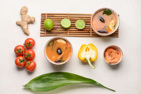 Bowls of spicy Thai soup with ingredients on light background