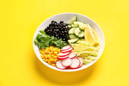Bowl with ingredients for Mexican vegetable salad on yellow background