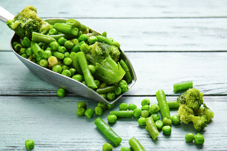 Scoop with frozen green vegetables on wooden backgroundの写真素材