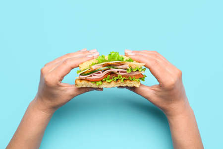 Female hands with tasty sandwich on color backgroundの写真素材