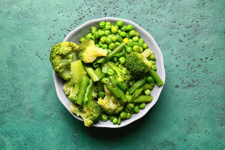 Bowl with frozen green vegetables on color background