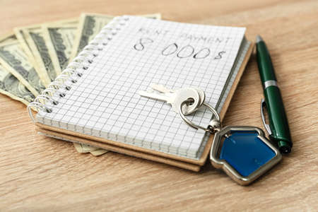 Notebook, pen, money and key with house shaped keychain on wooden background, closeupの写真素材