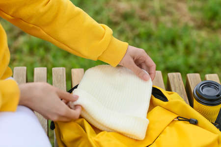 Woman holding beanie hat near backpack outdoors, closeup