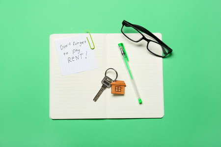 Opened notebook with text DON'T FORGET TO PAY RENT, eyeglasses, pen and key with keychain on color backgroundの写真素材