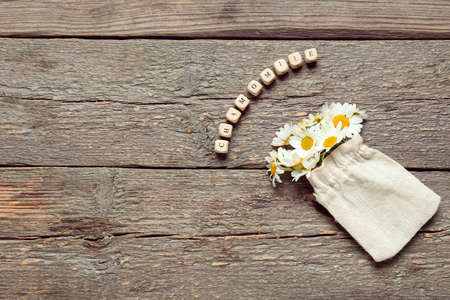 Bag with beautiful chamomile flowers with text CHAMOMILE on wooden backgroundの写真素材