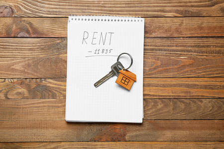 Notepad with word RENT and key with house shaped keychain on wooden backgroundの写真素材
