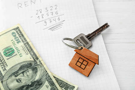 Key from house with keychain, money and notepad with rent calculation on white wooden background, closeupの写真素材