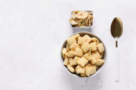 Bowl with tasty corn pillows and banana chips on light background