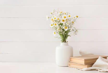 Vase with beautiful chamomile flowers and books on light wooden backgroundの写真素材