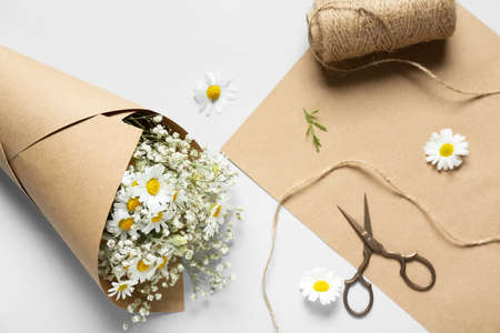 Bouquet of beautiful chamomile flowers, rope and scissors on light backgroundの写真素材