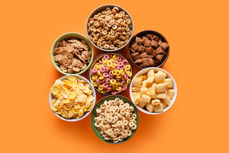 Bowls with different cereals on color background