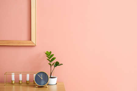 Stylish alarm clock with candles and houseplant on table near pink wall background