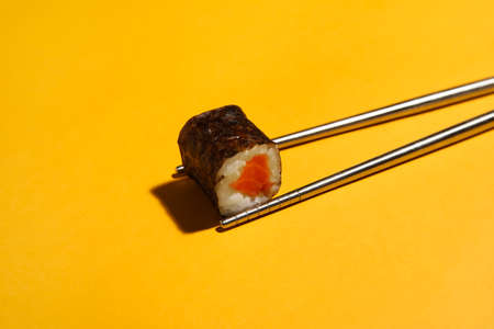 Chopsticks with salmon sushi roll on color background