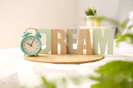 Stylish alarm clock with wooden word DREAM on bed