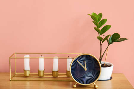 Stylish alarm clock with candles and houseplant on table near pink wall backgroundの写真素材