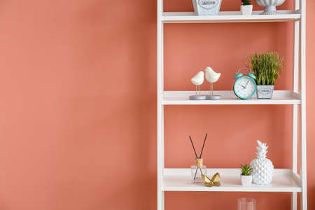 Bookshelf with alarm clock and different decor near pink wall
