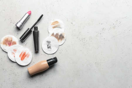 Lipstick, mascara, foundation and used cotton pads on light background